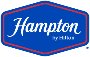 Logo for Hampton by Hilton featuring white text on a blue shield-shaped background with a red border.